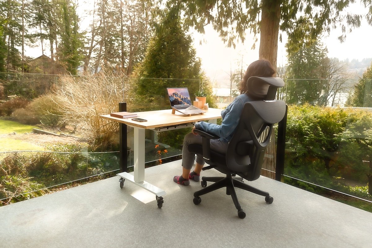 Personne assise à un bureau avec un ordinateur portable, entourée d'une vue forestière.