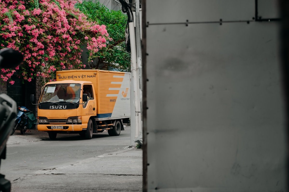 Camion de livraison jaune dans une ruelle fleurie.