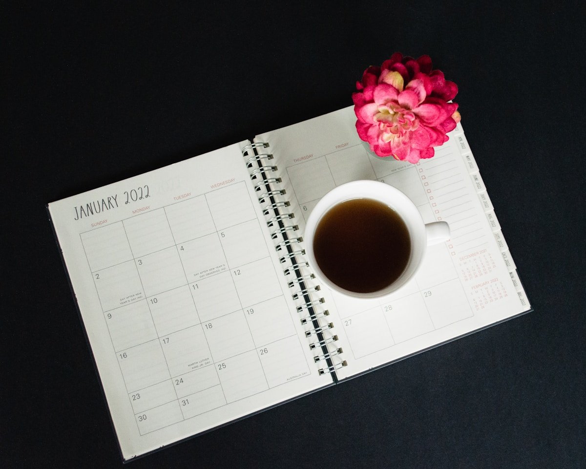 Calendrier de janvier 2022, tasse de café et fleur rose sur fond noir.