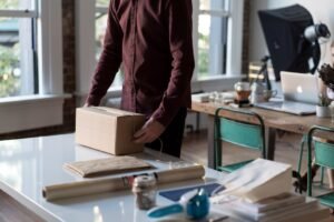 Person tenant une boîte en carton sur une table, représentant les avantages d'externaliser la livraison de vos meubles pour u