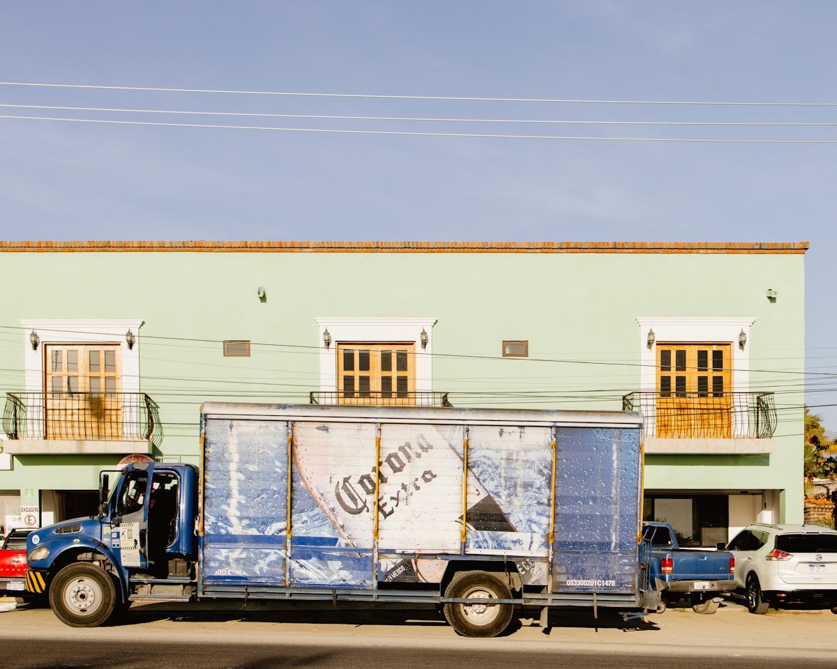 Bâtiment coloré avec fenêtres, camion de livraison et voitures garées.