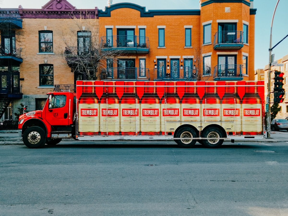 Camion rouge transportant des bouteilles de bière Tremblay dans une ville.