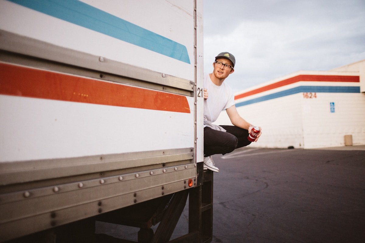 Homme souriant assis sur le côté d'un camion de livraison.