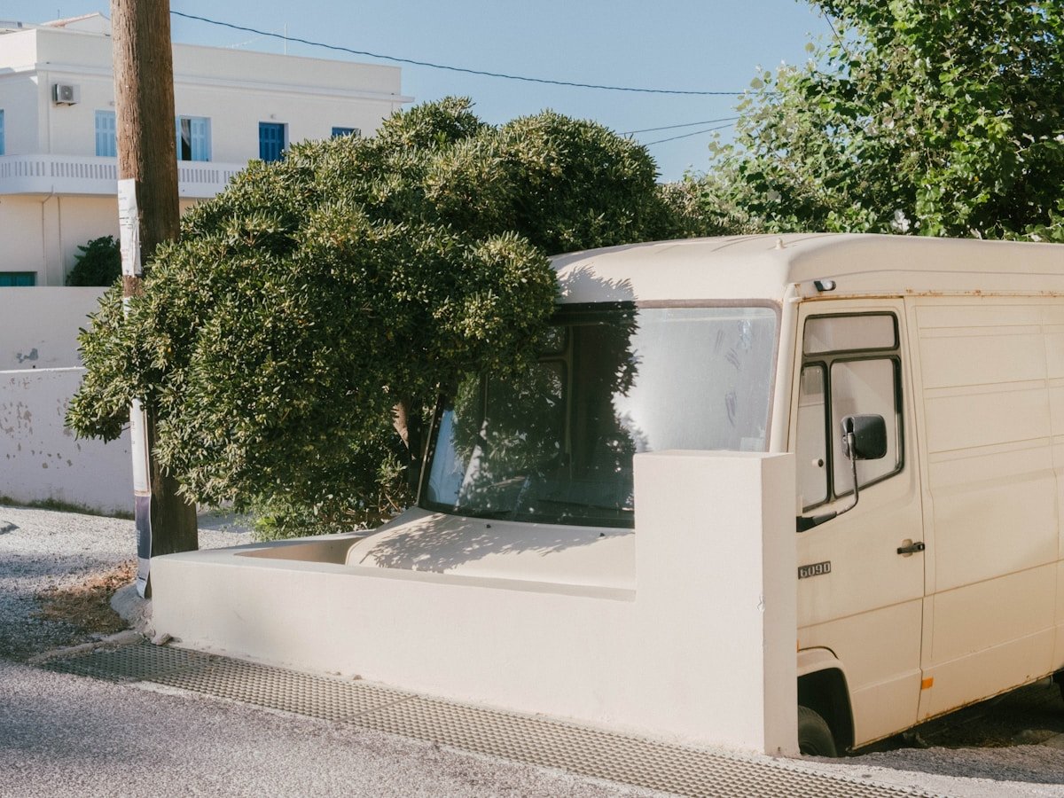 Camionnette blanche garée dans une rue ombragée par des arbres.
