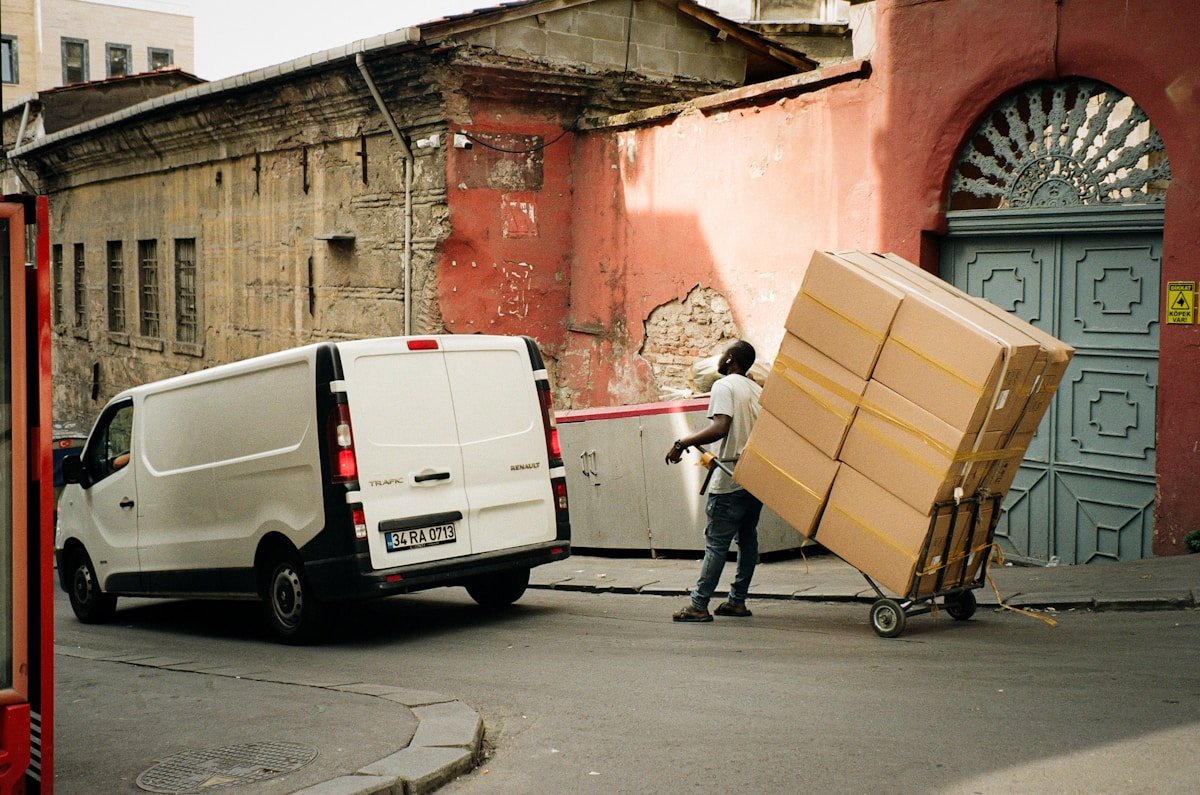 Camion de livraison, cartons empilés, homme poussant un chariot, bâtiment délabré.