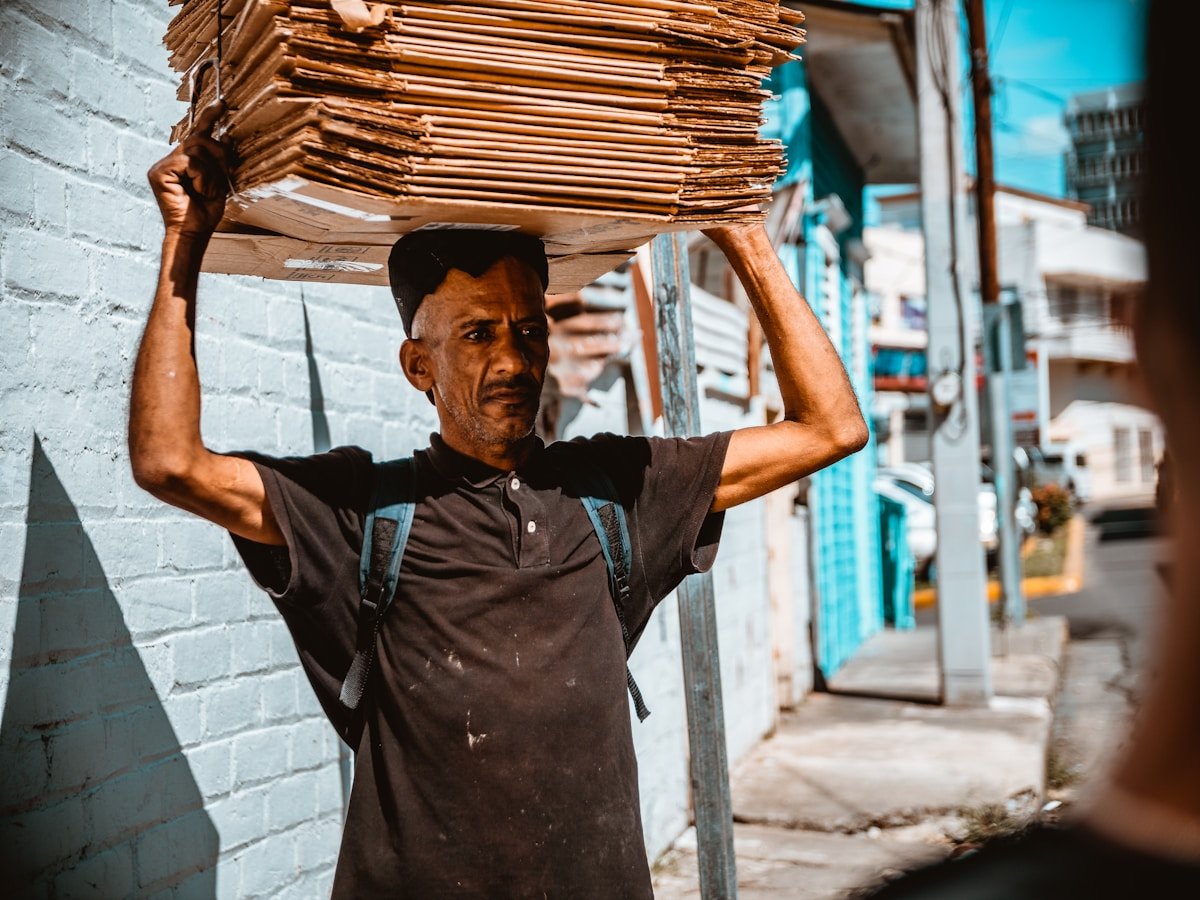 Homme portant une lourde charge de planches de bois sur la tête.