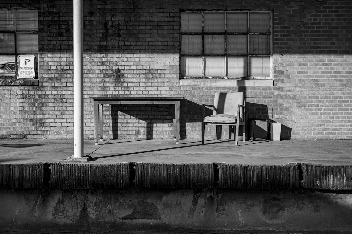 Bâtiment en briques, tables et chaises abandonnées, ombre et lumière contrastées.