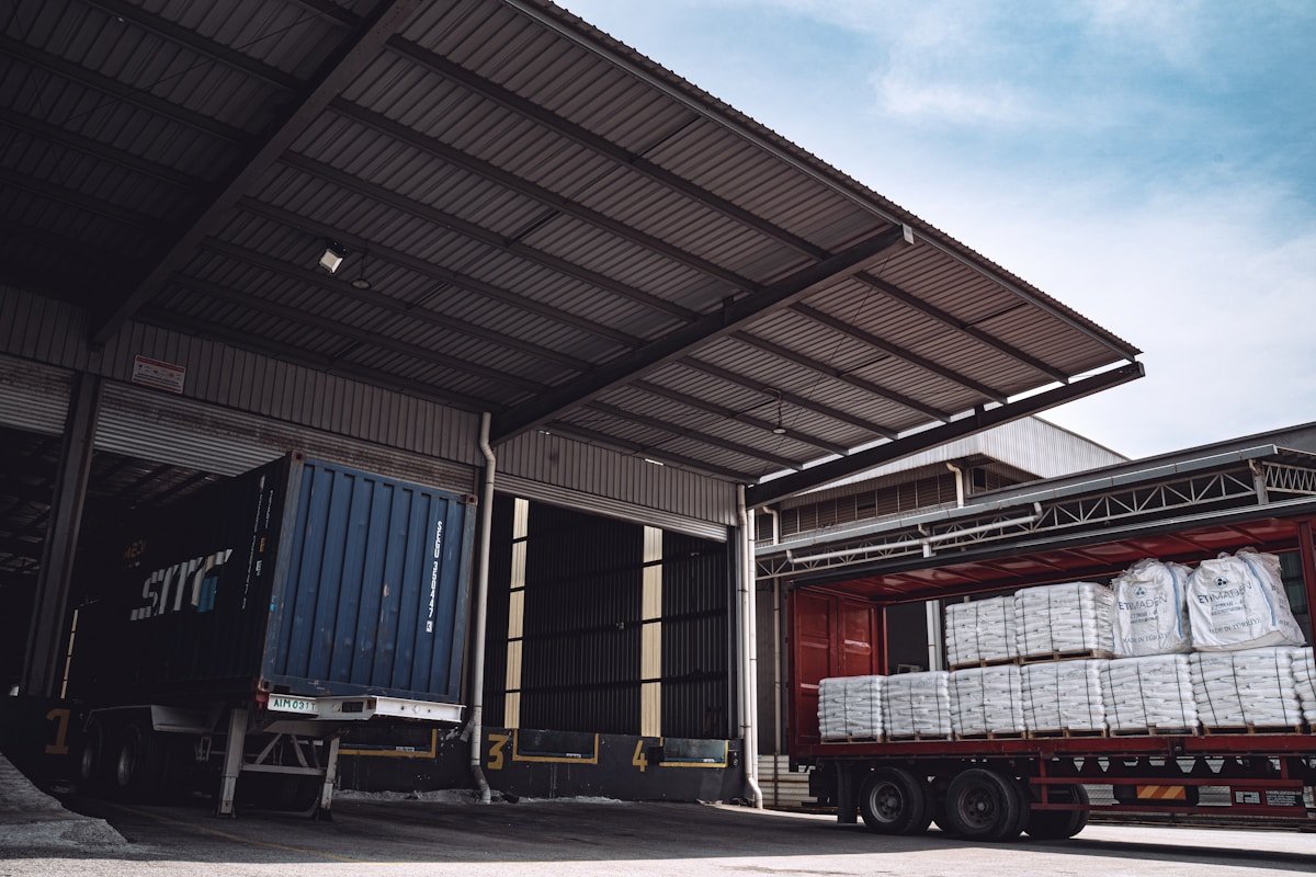 Entrepôt industriel avec conteneurs et camions de livraison.