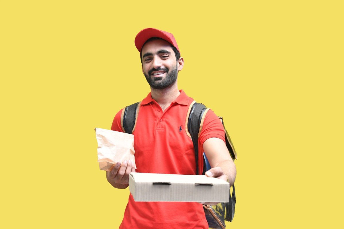 Livreur souriant en uniforme rouge tenant un colis.