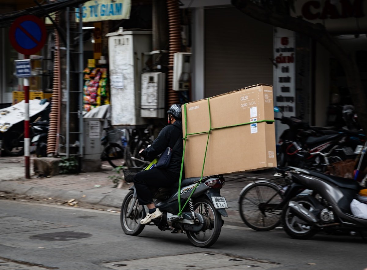 Livreur sur moto transportant un colis volumineux dans une rue animée.