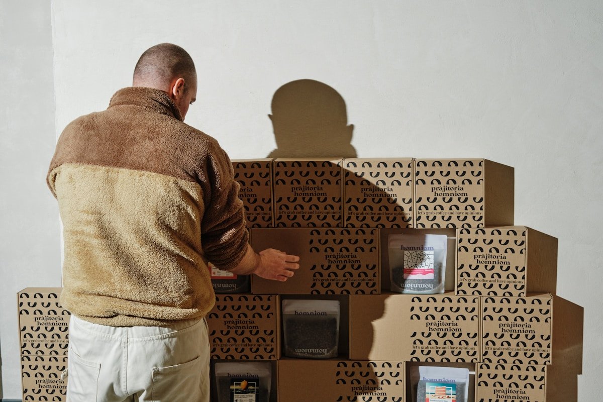 Homme debout devant des boîtes imprimées avec un motif répétitif.
