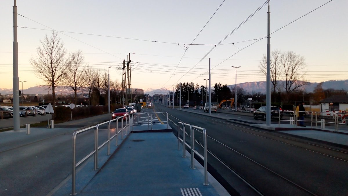Voie de tramway urbaine avec arbres nus et montagnes à l'horizon.
