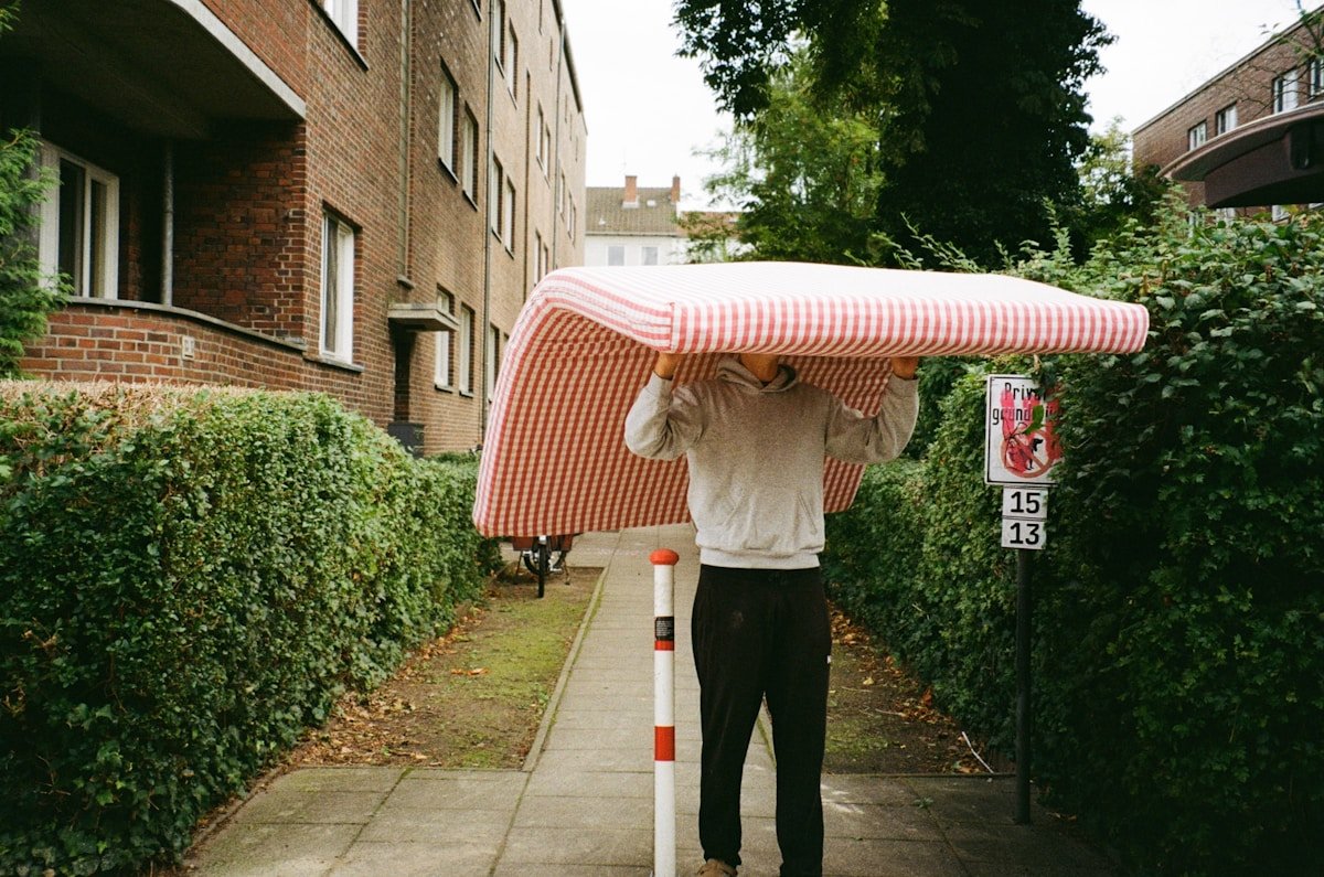 Personne portant un matelas rayé rose et blanc dans la rue.