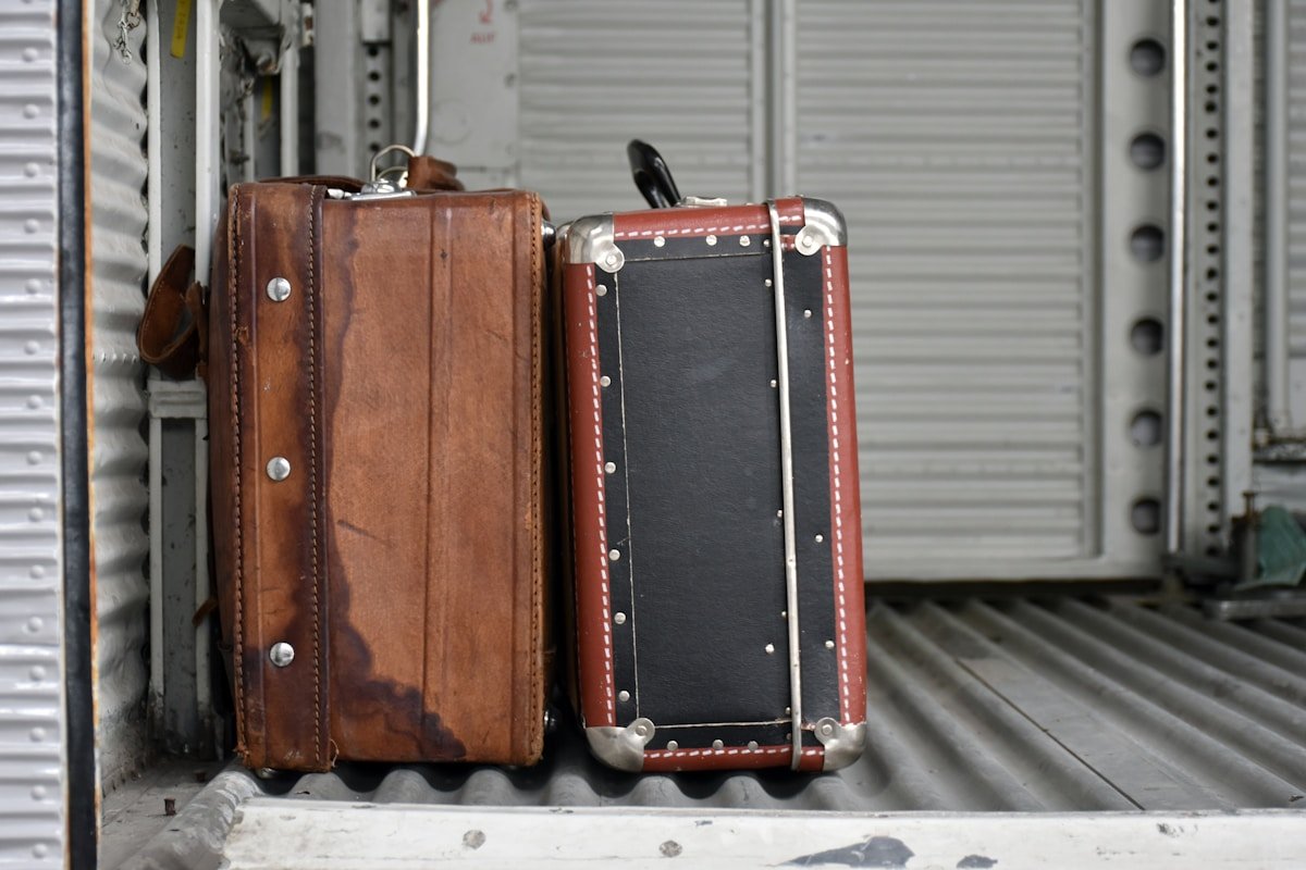 Deux valises vintage en cuir brun et noir, posées sur un sol métallique.