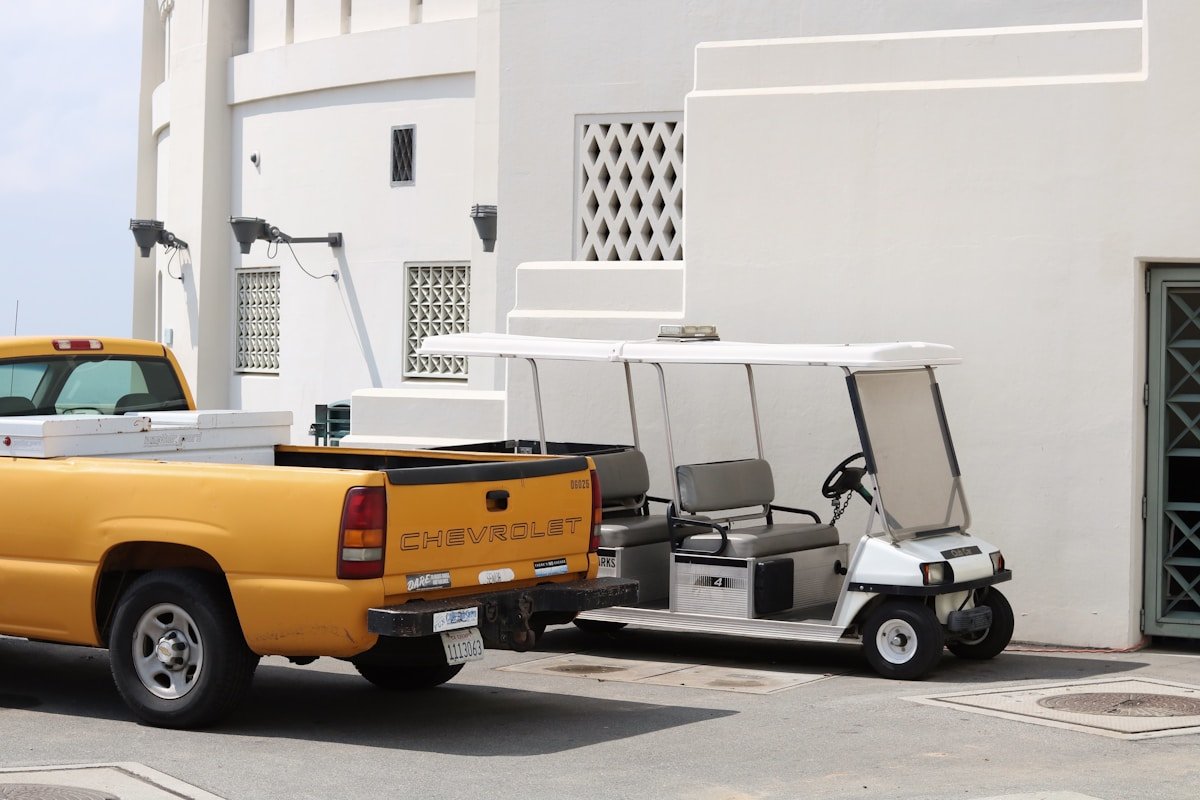 Camionnette Chevrolet jaune, chariot de golf blanc, bâtiment blanc avec fenêtres.