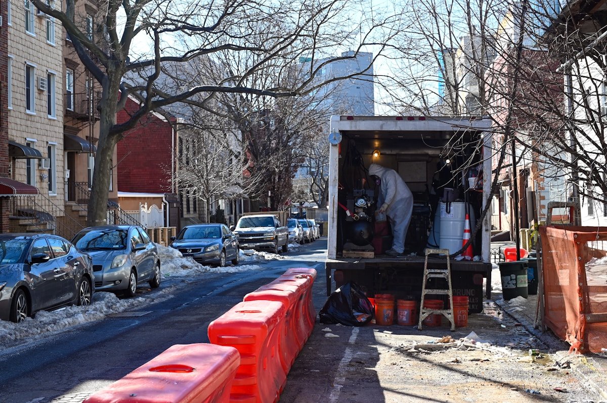 Rue urbaine enneigée avec voitures, barricades rouges et travaux en cours.