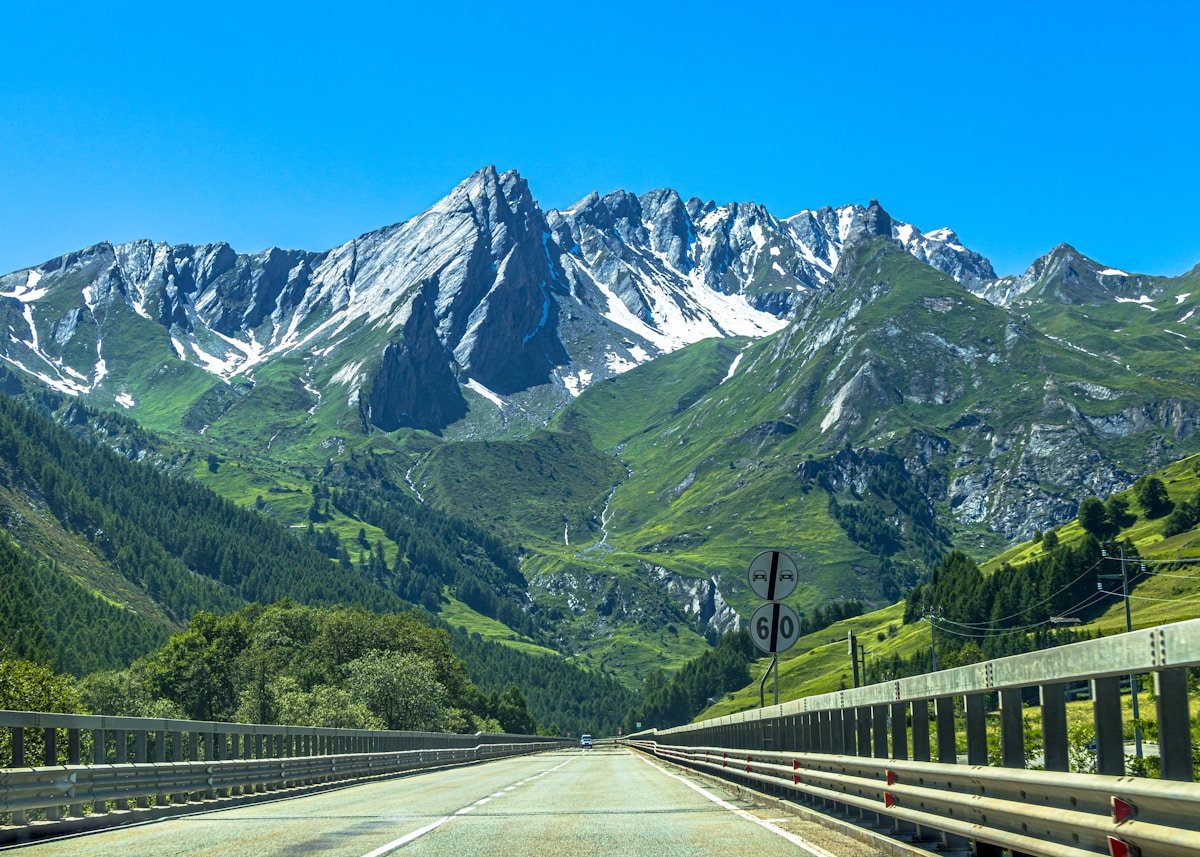 Paysage montagneux enneigé avec forêt verdoyante et route sinueuse.