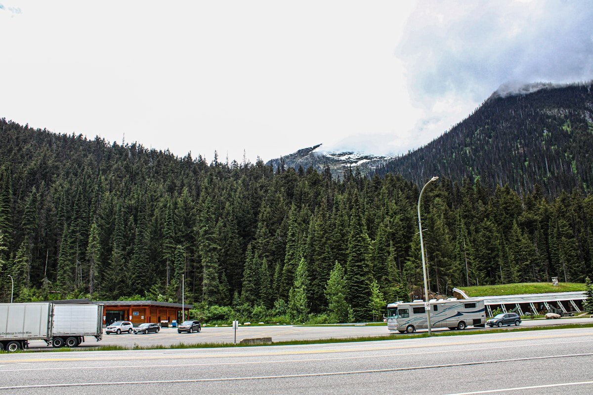 Paysage montagneux boisé avec véhicules et bâtiments sur la route.