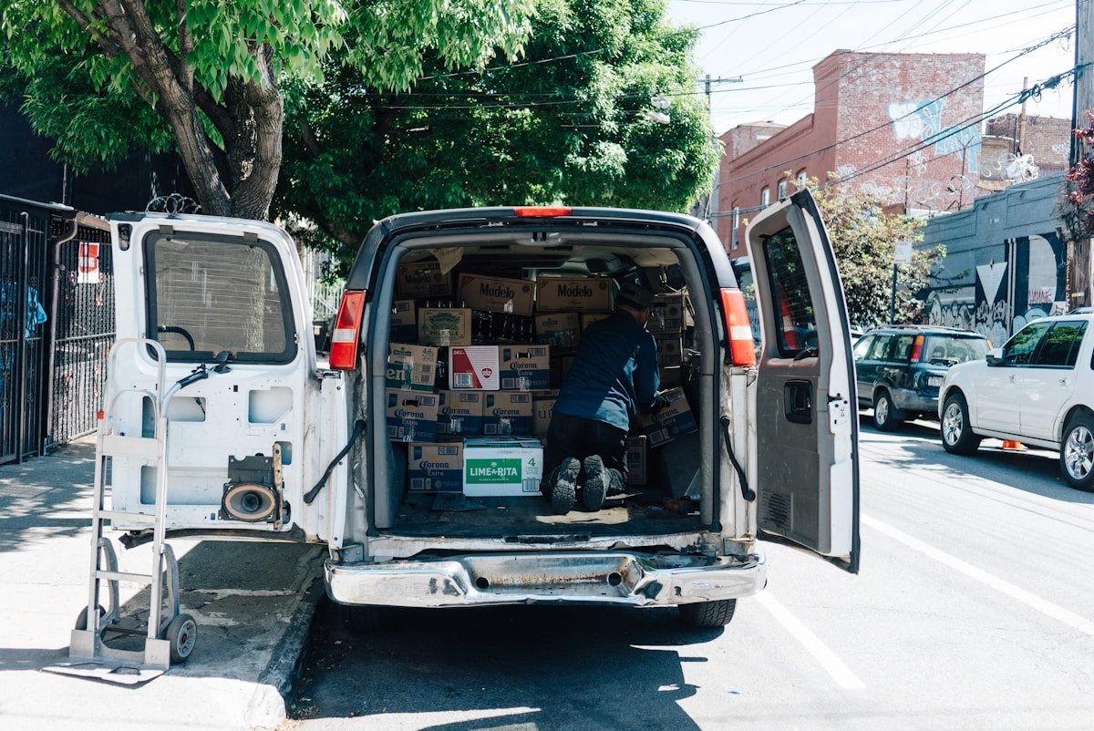 Camionnette blanche remplie de boîtes de bière Corona sur une rue urbaine.