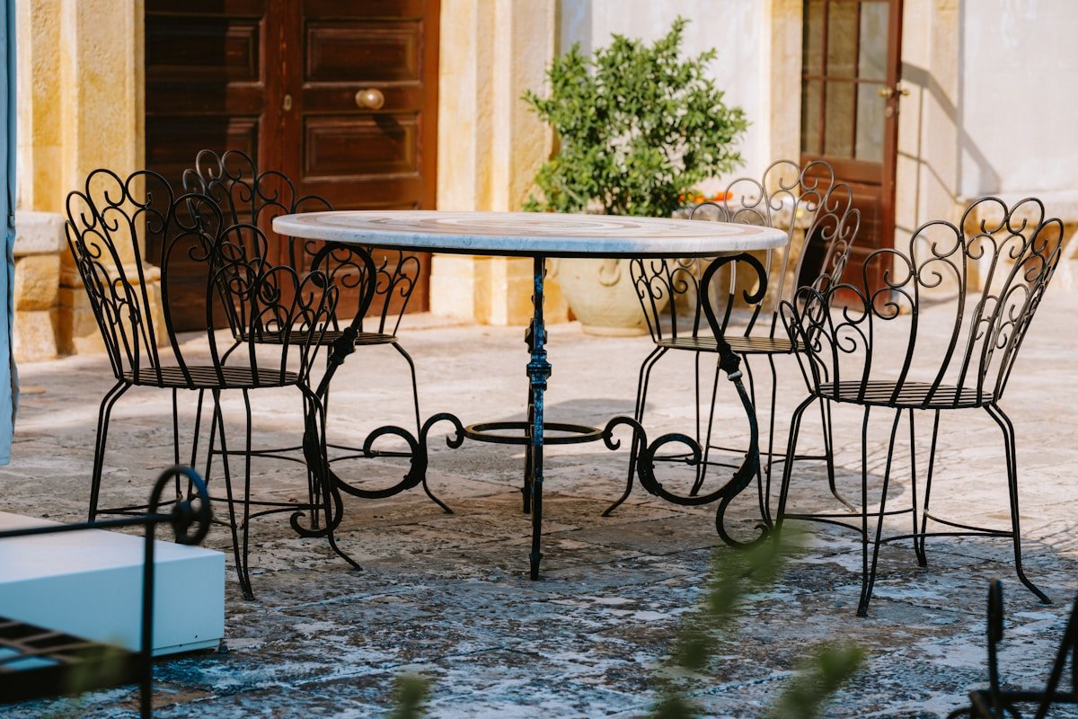 Table ronde en fer forgé avec chaises assorties dans une cour pavée.
