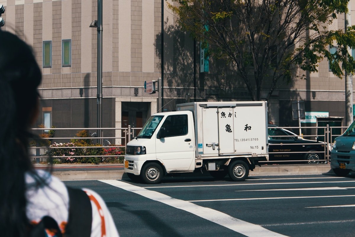 Camion de livraison blanc stationné dans une rue urbaine avec des arbres.