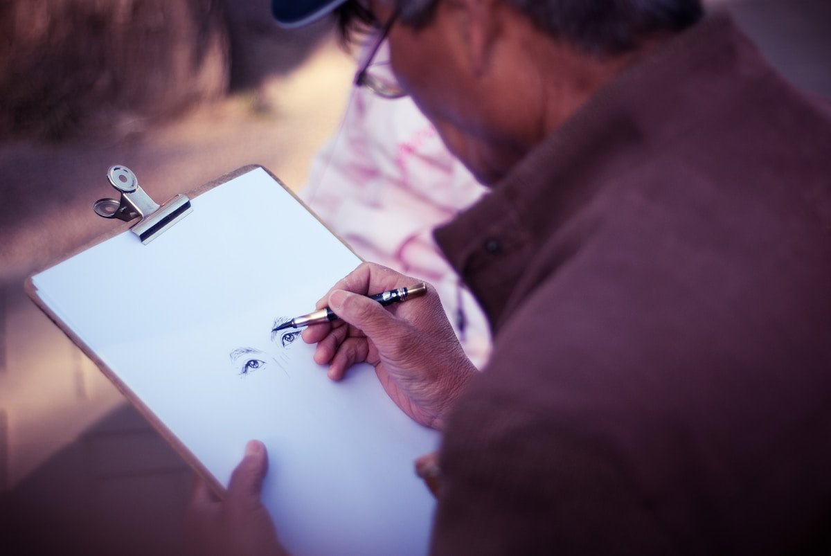 Gros plan des mains d'un artiste dessinant un visage sur un bloc-notes.