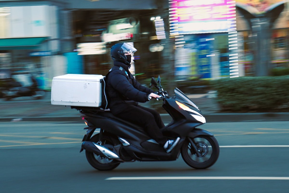 Livreur sur un scooter noir dans une ville animée la nuit.