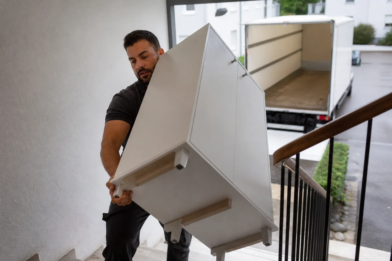 Un homme portant des vêtements noirs transporte un meuble blanc encombrant.