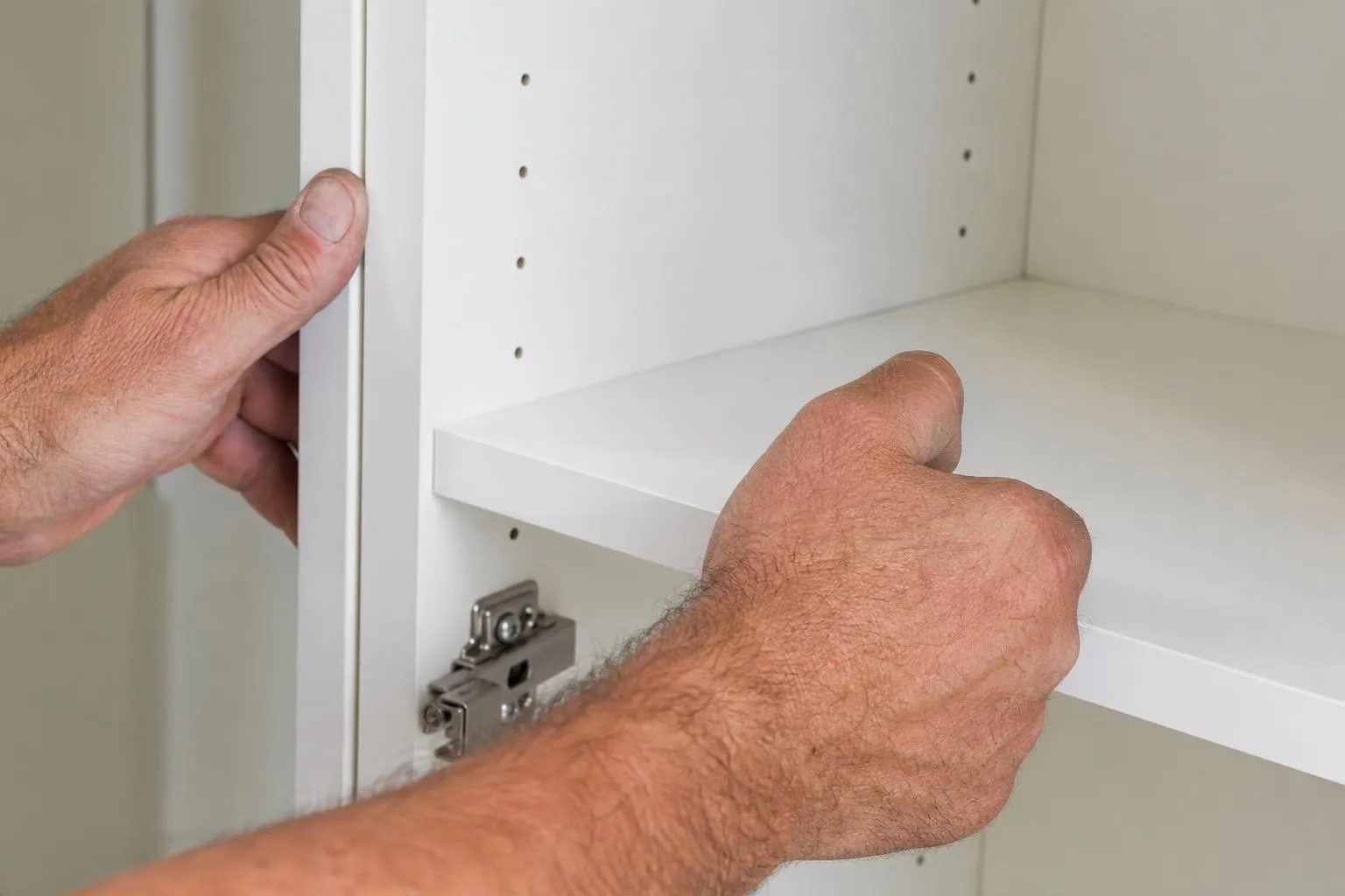 Mains installant une étagère blanche avec des trous de fixation.