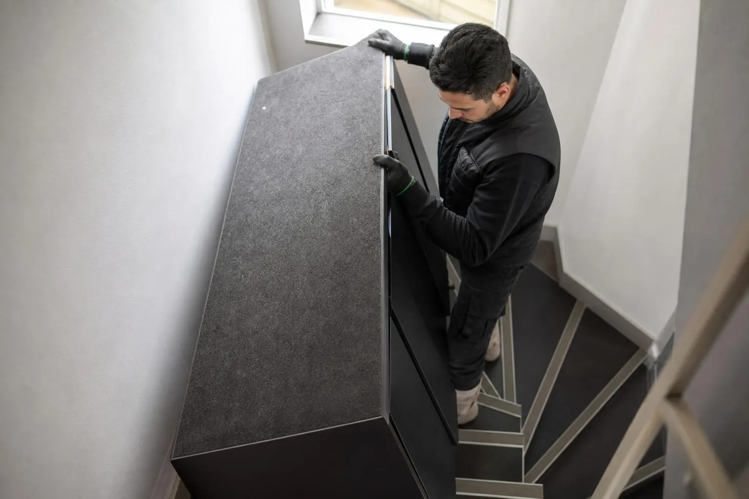 Un homme installant un meuble gris dans un escalier.
