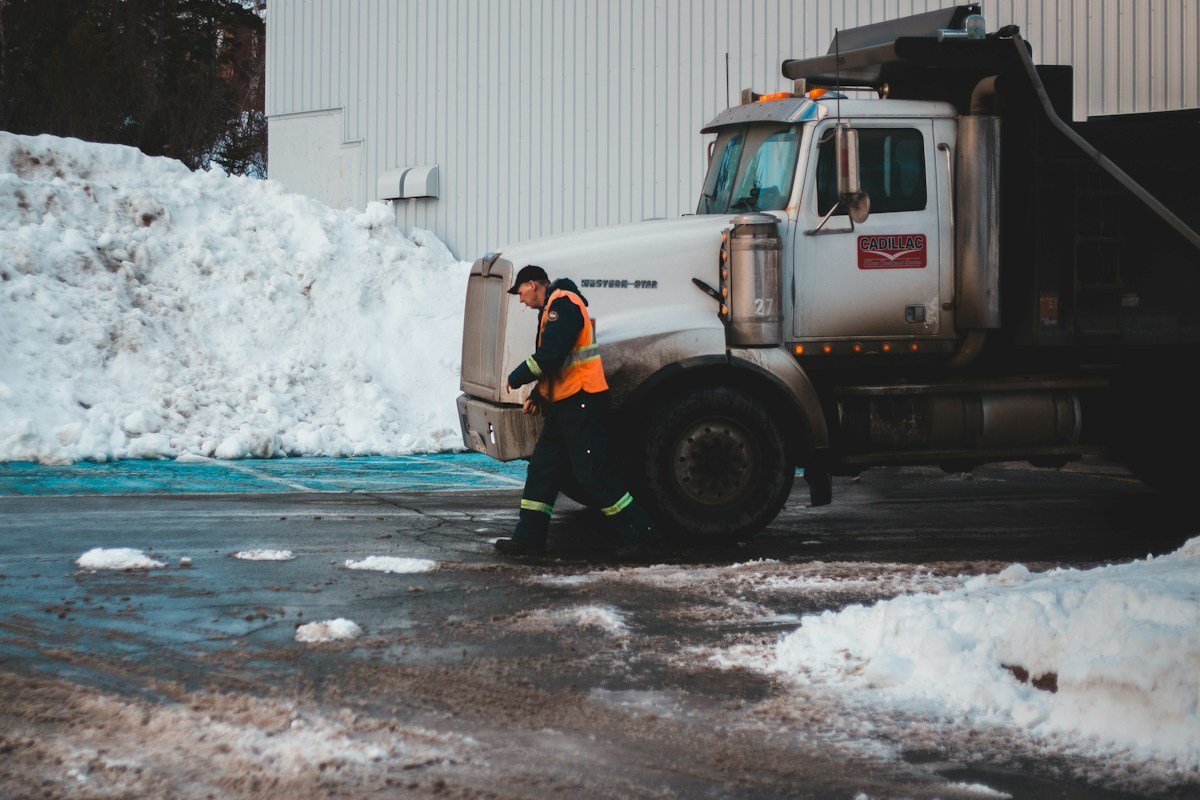 Camion-benne et ouvrier déneigeant devant un bâtiment enneigé