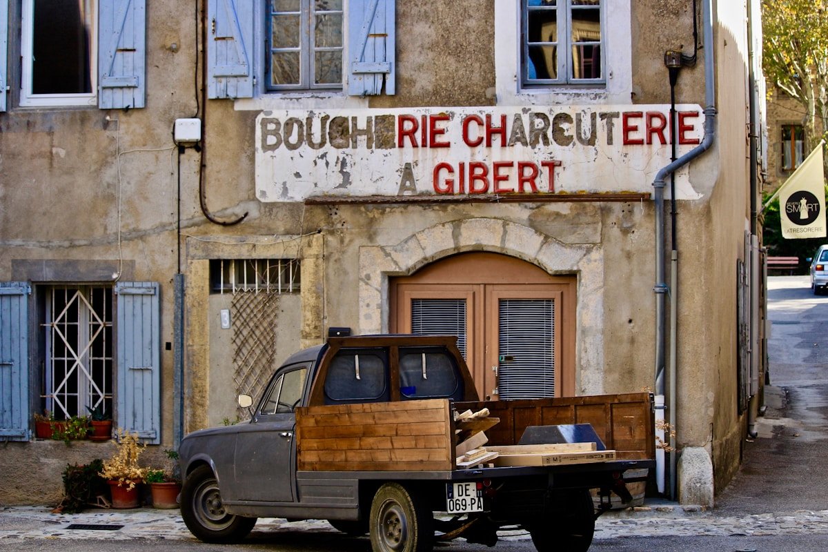 Boucherie charcuterie Gibert, vieux bâtiment, camion de livraison, rue pavée, détails architecturaux.